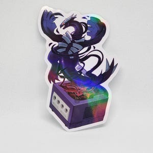 May include: Holographic sticker featuring a stylized black and purple dragon emerging from a purple GameCube console. The dragon has sharp claws and wings, with rainbow-colored accents. The sticker has a glossy finish.