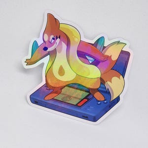 May include: Holographic sticker featuring a cartoon character with a fox-like appearance, in shades of orange, yellow, and purple. The character is standing on a blue handheld gaming device. The sticker has a glossy, iridescent finish.