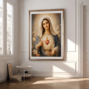May include: A framed wall art print depicting a figure with a veil and blue mantle, featuring a glowing heart with a cross and sword at the center. The figure is surrounded by a soft golden halo and white lilies, set against a light background.