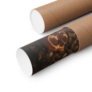 Op de afbeelding: Twee opgerolde posters in bruine kartonnen kokers. E&eacute;n poster is gedeeltelijk uitgerold en toont een gedetailleerde illustratie van een doormidden gesneden granaatappel, met zijn rode zaden. De achtergrond is donker met bladeren.