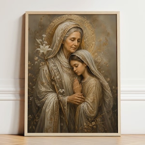 May include: A framed wall art print depicting an older woman and a younger girl wearing veils and robes in shades of gold, beige, and cream. The older woman holds a white lily staff, and both figures have golden halos against a soft, floral background.