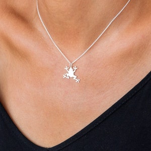 May include: A silver necklace with a frog pendant. The necklace is worn by a person with a black tank top.