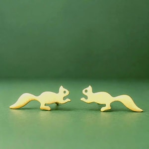 May include: A pair of gold-toned metal stud earrings shaped like squirrels. Each earring features a smooth, flat silhouette of a squirrel in a running pose with a bushy tail extended behind it, showcasing a clean and simple metallic finish.