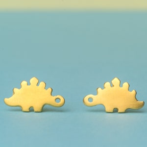 Könnte beinhalten: Ein Paar goldfarbene Ohrringe in Dinosaurierform. Die Ohrringe sind klein und zart und wären ein tolles Geschenk für einen Dinosaurier-Liebhaber.