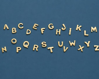 Op de afbeelding: Goudkleurige alfabetletters op een donkerblauwe achtergrond. De letters zijn in een schreeflettertype en zijn verspreid over het oppervlak. De letters zijn in hoofdletters en kleine letters.