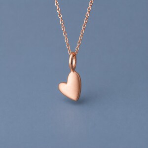 Può includere: Un ciondolo a forma di cuore color oro rosa sospeso a una delicata catenina a maglie abbinata. Il ciondolo a cuore presenta una finitura liscia e opaca con bordi arrotondati, appeso verticalmente a un piccolo anello circolare di giunzione.