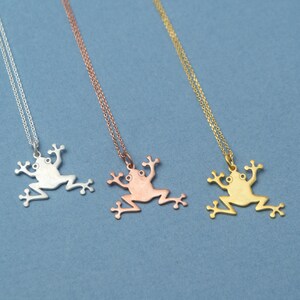 May include: Three silver frog necklaces on a blue background. The necklaces are in silver, rose gold, and gold.