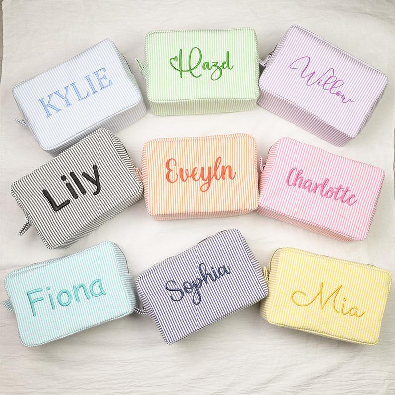 May include: Nine rectangular zippered pouches in various pastel and neutral striped fabrics, each featuring a unique embroidered name including Kylie, Hazel, Willow, Lily, Evelyn, Charlotte, Fiona, Sophia, and Mia in coordinating thread colors.