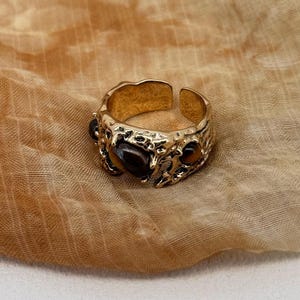 Puede incluir: Un anillo de oro con un diseño texturizado y tres piedras de color marrón oscuro.