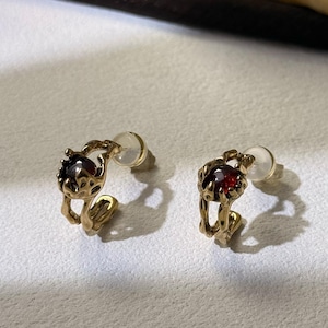 Könnte beinhalten: Ein Paar goldene Creolen mit einem roten Edelstein in der Mitte jedes Creolen.