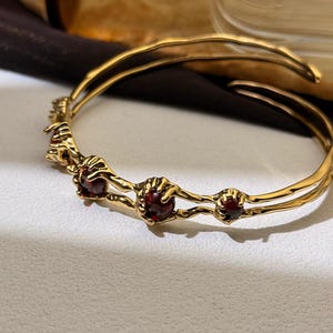 Peut inclure: Un bracelet jonc en or avec un design à double bande. Le bracelet est orné de cinq pierres précieuses rouges serties dans des griffes en or.