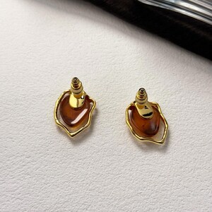 May include: A pair of gold earrings with a brown, teardrop-shaped stone set in a gold frame.