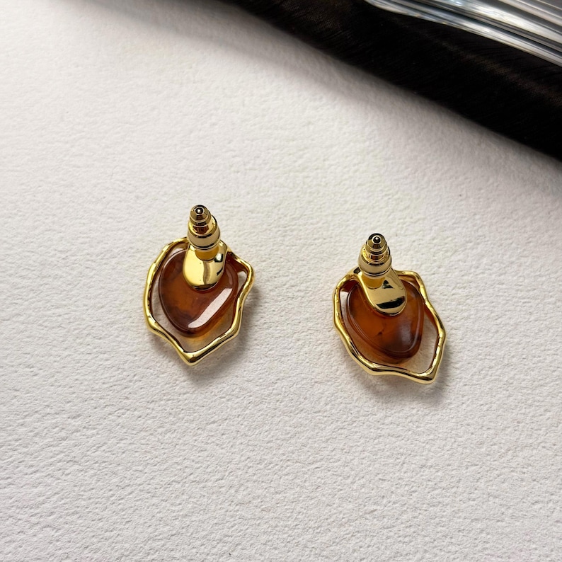 May include: A pair of gold earrings with a brown, teardrop-shaped stone set in a gold frame.