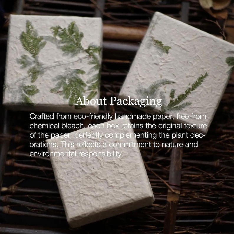 Handmade paper gift boxes featuring delicate green fern leaves embedded in the textured surface, resting on a wooden background. The boxes have a natural and rustic aesthetic, perfect for eco-friendly or vintage-inspired gift presentations.