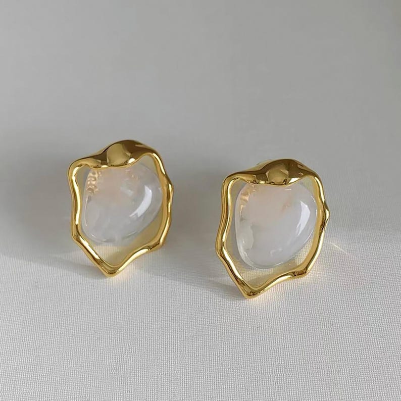 May include: A pair of gold earrings with a white, opaque, irregular shaped stone set in each earring.