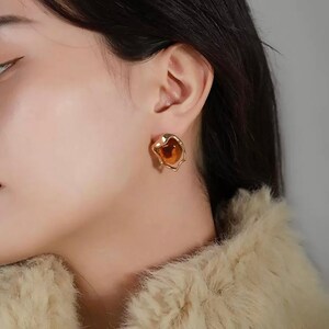 May include: Gold tone earrings with a brown, irregular shaped, resin stone.