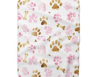 May include: White pet blanket with a repeating pattern of gold paw prints, pink paw prints, and gold bones. The blanket is soft and plush, perfect for a dog or cat.