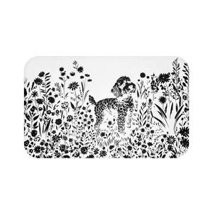 May include: A rectangular white bath mat featuring a black and white illustration. The design includes a poodle standing in a field of stylized flowers and foliage. The artwork is a monochromatic, botanical-themed design.