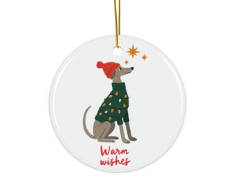 May include: A round, white Christmas ornament with a gold string. The ornament features a cartoon dog wearing a green sweater with lights and a red hat. The words "Warm wishes" are written in red.