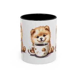 Puede incluir: Taza de café de cerámica blanca con interior negro. La taza presenta una ilustración de acuarela de un cachorro de Pomerania marrón claro y esponjoso sosteniendo una taza de café. El cachorro está sonriendo y la taza de café tiene manchas marrones.