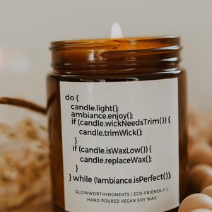 May include: A brown glass candle jar with a white label that reads "do { candle.light(); ambiance.enjoy(); if (candle.wickNeedsTrim()) { candle.trimWick(); } if (candle.isWaxLow()) { candle.replaceWax(); } } while (!ambiance.isPerfect()); GLOWWORTHYMOMENTS | ECO-FRIENDLY | HAND POURED VEGAN SOY WAX". The candle is lit and the flame is visible. The jar is sitting on a wooden surface.