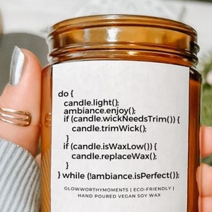 May include: A brown glass candle jar with a white label. The label has the text "do { candle.light(); ambiance.enjoy(); if (candle.wickNeedsTrim()) { candle.trimWick(); if (candle.isWaxLow()) { candle.replaceWax(); } } while (!ambiance.isPerfect()); GLOWWORTHYMOMENTS | ECO-FRIENDLY | HAND POURED VEGAN SOY WAX" printed on it.