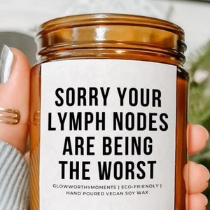 May include: A brown glass candle with a white label that reads "Sorry your lymph nodes are being the worst." The label also includes the text "GlowworthyMoments | Eco-Friendly | Hand Poured Vegan Soy Wax."