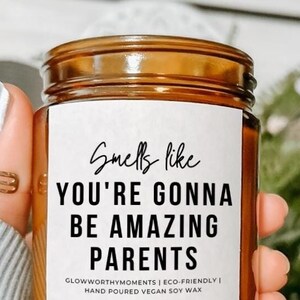 May include: A brown glass candle jar with a white label that reads "Smells like YOU'RE GONNA BE AMAZING PARENTS". The label also includes the text "GLOWWORTHYMOMENTS | ECO-FRIENDLY | HAND POURED VEGAN SOY WAX".