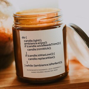 May include: A brown glass candle jar with a white label that reads "do { candle.light(); ambiance.enjoy(); if (candle.wickNeedsTrim()) { candle.trimWick() } if (candle.isWaxLow()) { candle.replaceWax(); } } while (ambiance.isPerfect()) GLOWWORTHYMOMENTS | ECO-FRIENDLY | HAND POURED | VEGAN SOY WAX"