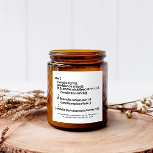 Op de afbeelding: Een bruine glazen kaars pot met een wit label waarop staat "do [ candle.light() ambiance.enjoy() if (candle.wickNeedsTrim()) candle.trimWick() if (candle isWaxLow()) candle.replaceWax() ] while (ambiance isPerfect()) GlowworthyAmbiance | Eco-Friendly | Hand Poured Vegan Soy Wax".