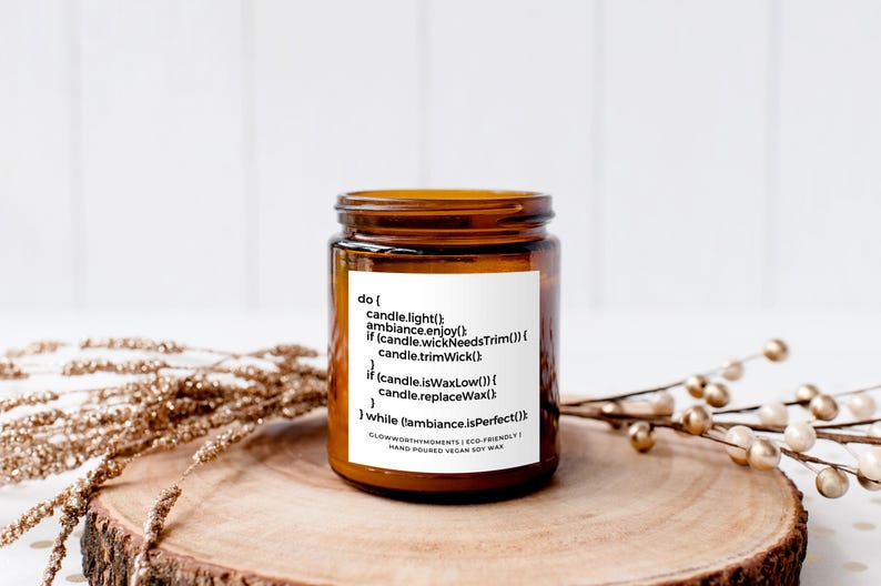 Op de afbeelding: Een bruine glazen kaars pot met een wit label waarop staat "do [ candle.light() ambiance.enjoy() if (candle.wickNeedsTrim()) candle.trimWick() if (candle isWaxLow()) candle.replaceWax() ] while (ambiance isPerfect()) GlowworthyAmbiance | Eco-Friendly | Hand Poured Vegan Soy Wax".