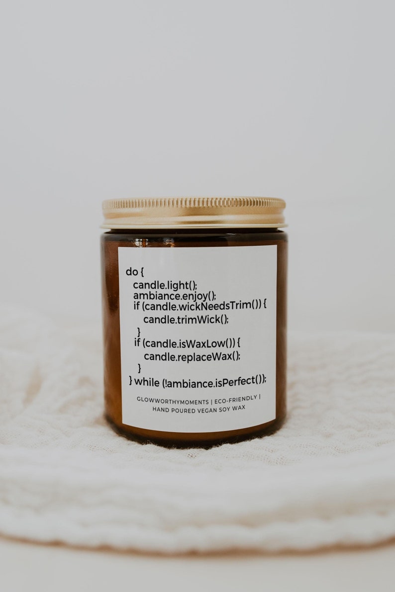 Op de afbeelding: Een bruine glazen kaars pot met een gouden deksel. Het etiket luidt "do { candle.light(); ambiance.enjoy(); if (candle.wickNeedsTrim()) { candle.trimWick(); } if (candle.isWaxLow()) { candle.replaceWax(); } } while (!ambiance.isPerfect()); GLOWWORTHYMOMENTS | ECO-FRIENDLY | HAND POURED VEGAN SOY WAX"