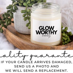 Op de afbeelding: Een witte kaars met een zwart label waarop "Glow Worthy moments" staat. De kaars staat op een houten dienblad met groene planten.