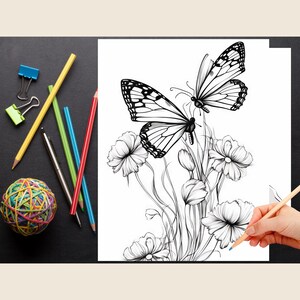 May include: A black and white line drawing of two butterflies perched on a cluster of flowers. The butterflies have intricate wing patterns and the flowers are detailed with delicate petals. The drawing is on a white sheet of paper and a hand is holding a blue pencil over the paper.