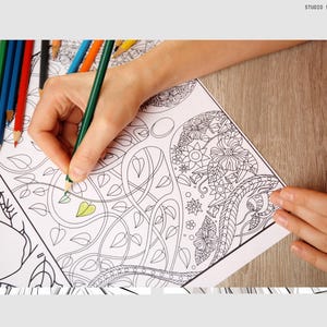May include: A person coloring in a detailed black and white drawing of flowers and leaves with colored pencils. The drawing is on a white sheet of paper.