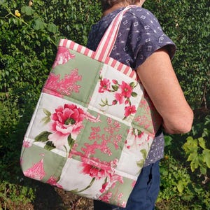 May include: A floral patterned tote bag. The bag has a patchwork design with large pink flowers, green leaves, and white backgrounds. The handles are striped in red and white.