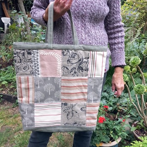 May include: A patchwork tote bag featuring a mix of floral and geometric patterns in shades of grey, pink, and white. The bag has two handles and a green trim.