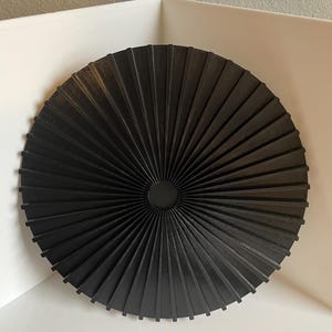 May include: A black circular wall decor with a sunburst design. The decor is made of thin, flat pieces of wood that radiate out from the center.