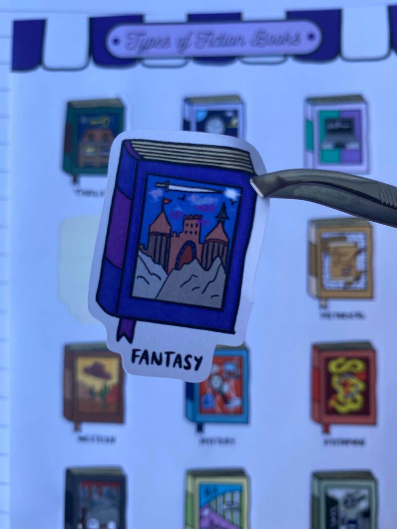 Detailed close up shot of a Fantasy book sticker. The sticker is Purple and Blue and features a beautiful castle. The sticker is held by a tweezer against a blurred background of the sticker sheet.