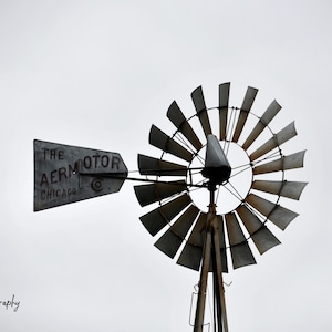 Puede incluir: Un molino de viento vintage de metal gris con el texto "The Aermotor Chicago" en el lateral. El molino de viento tiene un gran ventilador circular con muchas aspas.