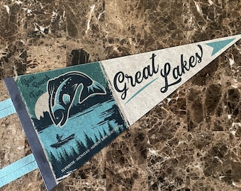 May include: A vintage-style pennant with the text "Great Lakes" in a cursive font. The pennant is blue and white with a graphic of a fish jumping out of the water. The text "Year Round Fun" is in the upper left corner. The text "Superior - Michigan - Huron - Erie - Ontario" is in the lower right corner.