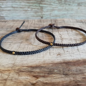 May include: Two braided cord bracelets with gold accents. The bracelets are black and brown.