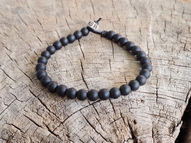 May include: A black beaded bracelet with a silver bead accent. The bracelet is made of matte black beads and has a simple design.