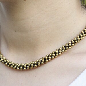May include: A gold necklace made of small, round beads. The beads are arranged in a spiral pattern.
