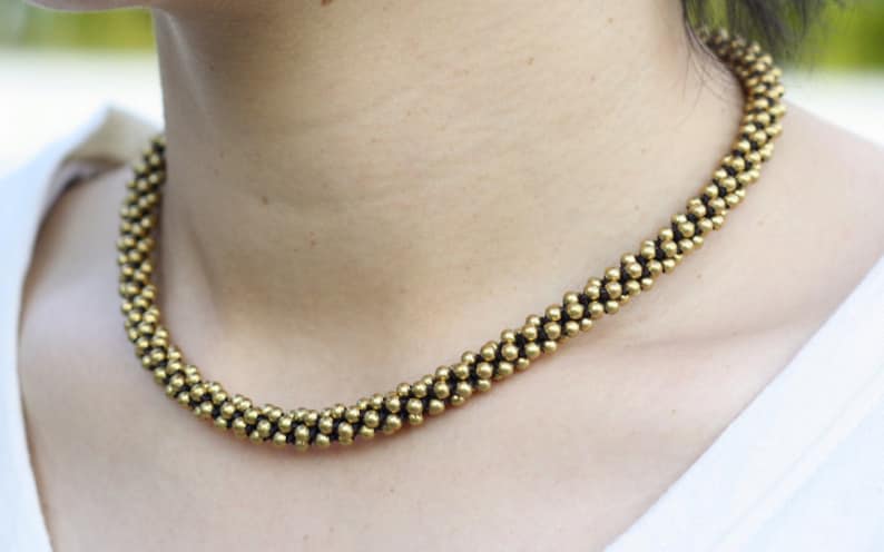 May include: A gold necklace made of small, round beads. The beads are arranged in a spiral pattern.