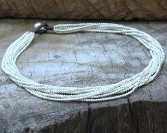 May include: A silver necklace with multiple strands of small beads. The necklace is laying on a wooden surface.