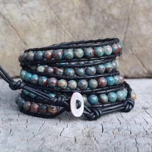 以下が含まれることがあります： 黒革の紐で巻かれた、青と茶色の模様のビーズが複数層になったブレスレット。ボタン留めです。
