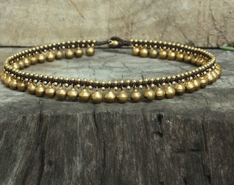May include: A gold anklet with a double row of small bells. The anklet is made of brown cord and has a simple design.