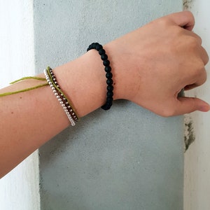 May include: A person's wrist wearing three bracelets. The top bracelet is black, the middle bracelet is brown and silver, and the bottom bracelet is green.