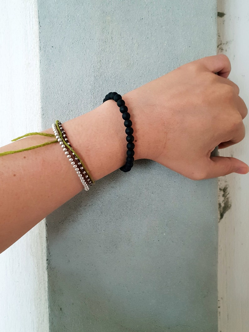 May include: A person's wrist wearing three bracelets. The top bracelet is black, the middle bracelet is brown and silver, and the bottom bracelet is green.